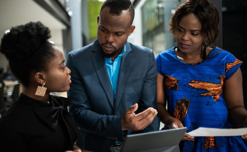 Focused group of young African businesspeople standing in the lobby of a modern office and talking together over a digital tablet